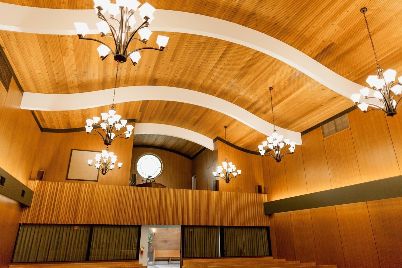 An interior view of a room with wood-paneled walls and a curved ceiling featuring several hanging chandeliers.