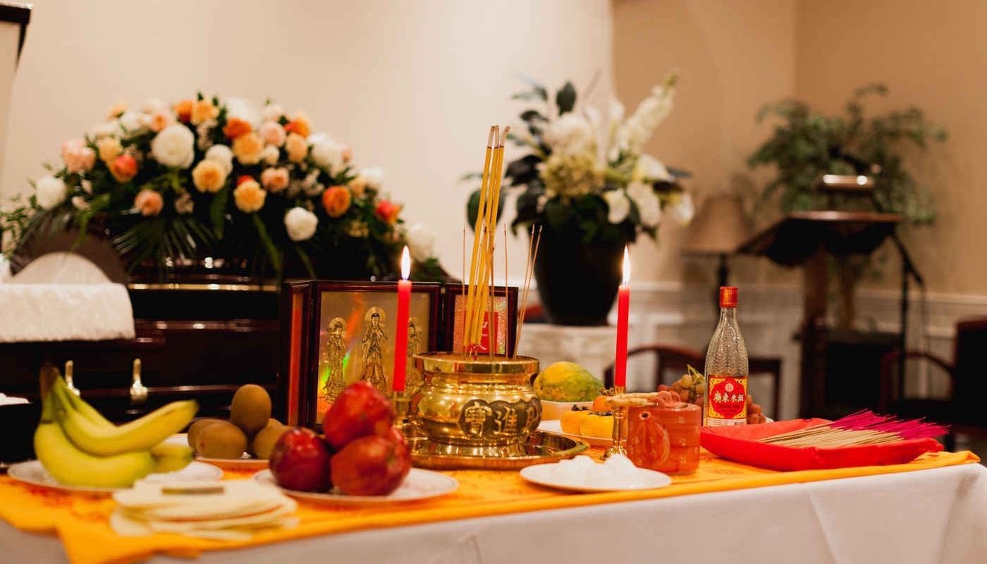 A table with fruit , candles , flowers and a coffin in the background.