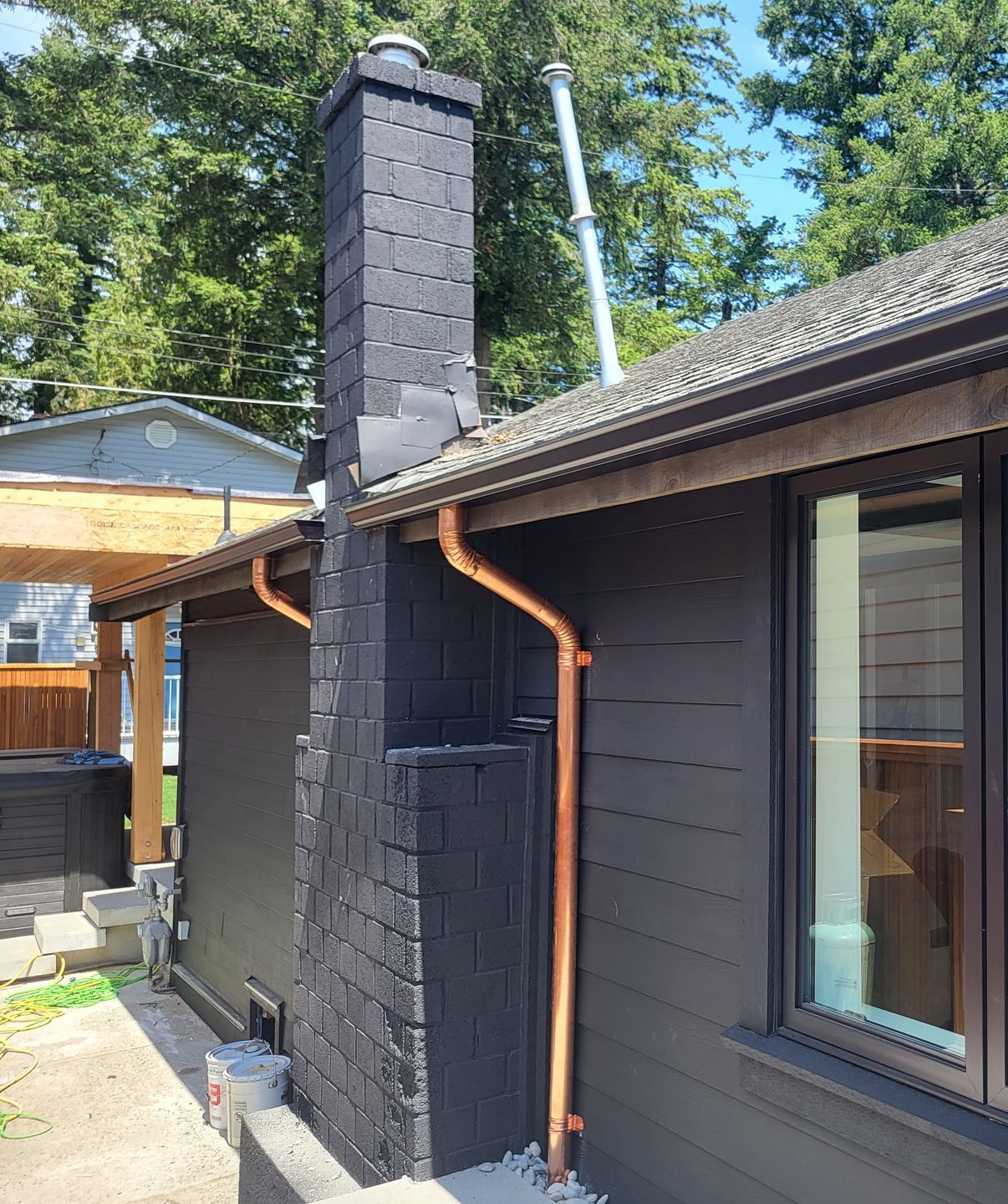 A dark-painted exterior wall with a matching brick chimney and a new, vertical copper downspout.