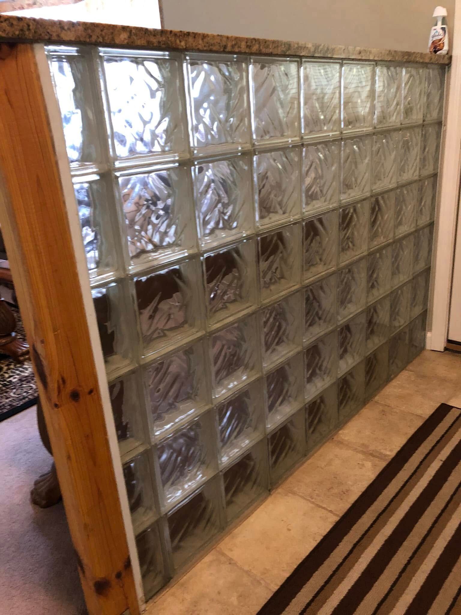A room divider wall made of clear glass blocks topped with a granite counter, framed by a wooden pillar on the left.