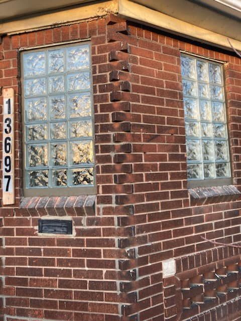 The exterior corner of a brick building with glass block windows and a vertical address sign reading 13697.
