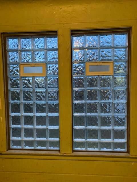 Two glass block windows set in a yellow wall, each featuring a small rectangular ventilation pane.