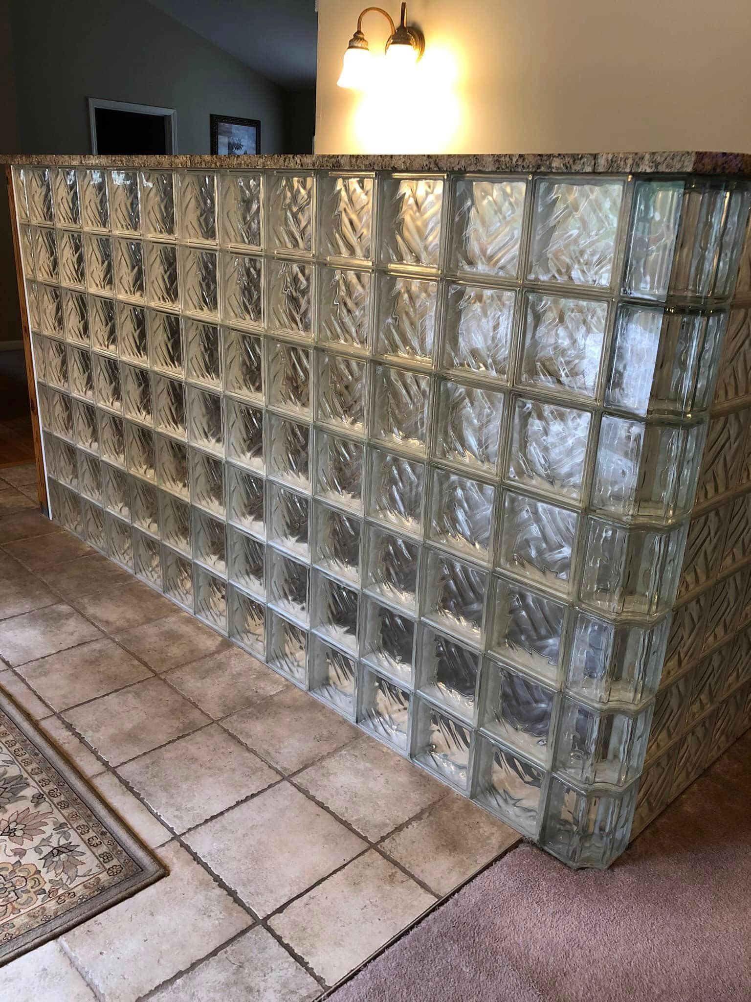 A waist-high partition wall made of textured glass blocks, topped with a granite counter, in a tiled indoor space.