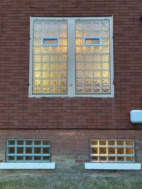 A red brick wall featuring two large upper windows with glass blocks and two smaller glass block basement windows below.