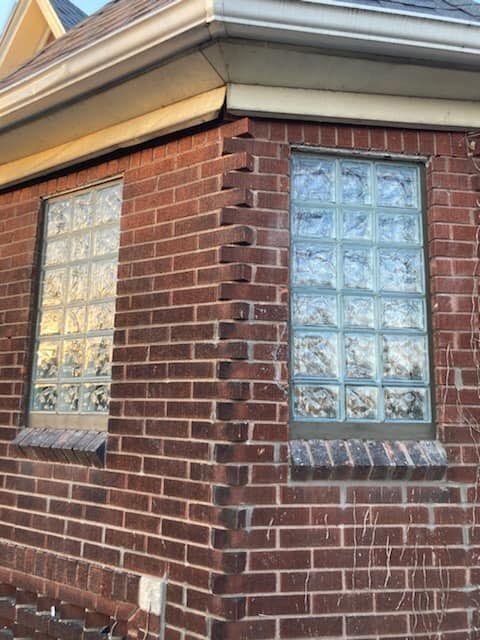 A corner of a red brick house with two rectangular windows featuring textured glass blocks.