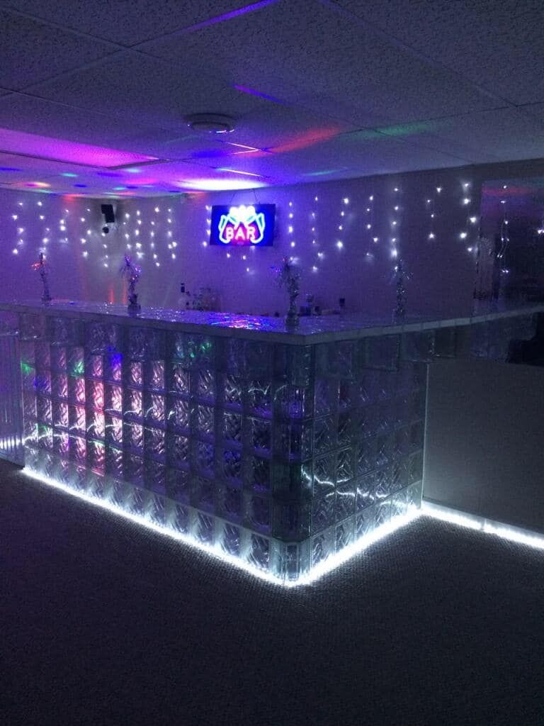 A glowing glass-block bar illuminated with LED lights, featuring string lights on the wall and a neon sign in a dark room.