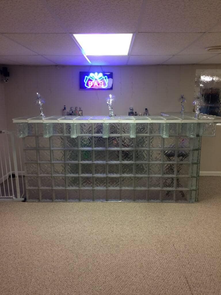 A home bar built from glass blocks in a carpeted basement with a neon 