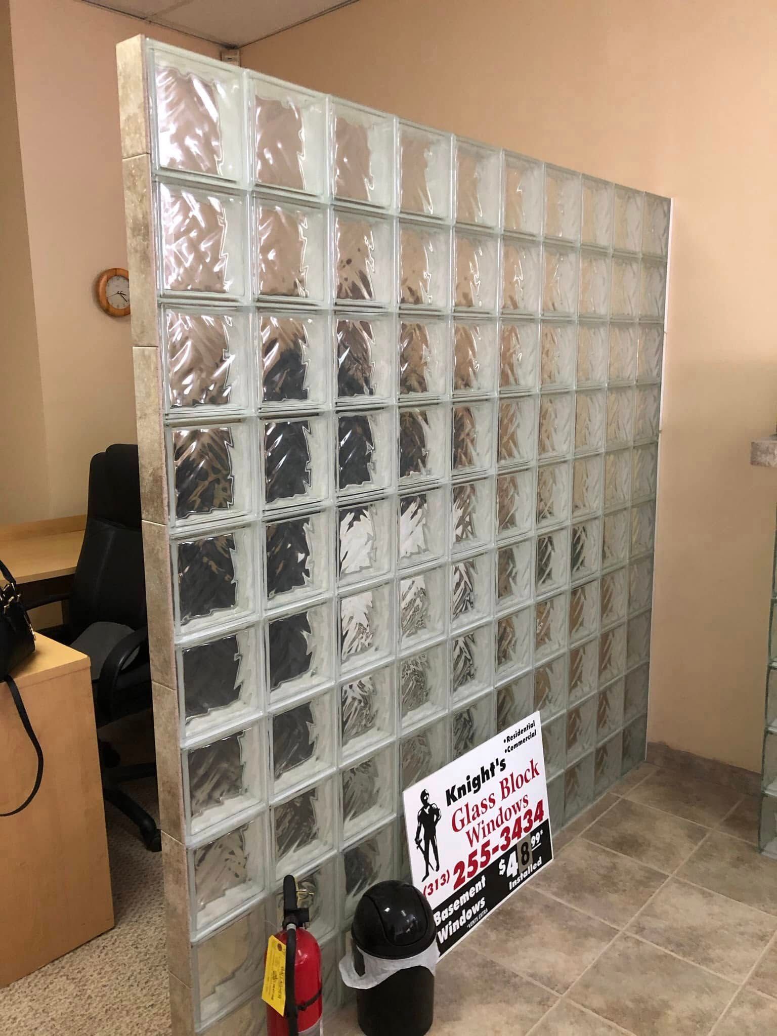 A freestanding glass block partition wall sits in an office space near a fire extinguisher and a sign.