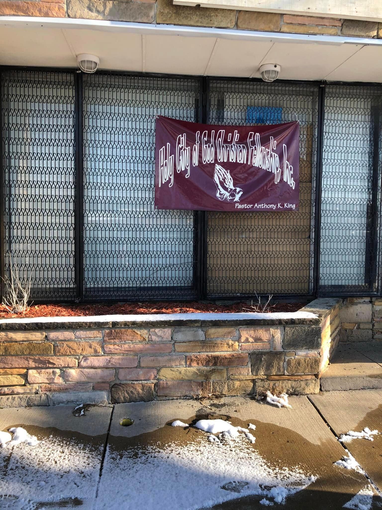 A storefront with metal security bars over the glass and a burgundy banner featuring white text and praying hands.