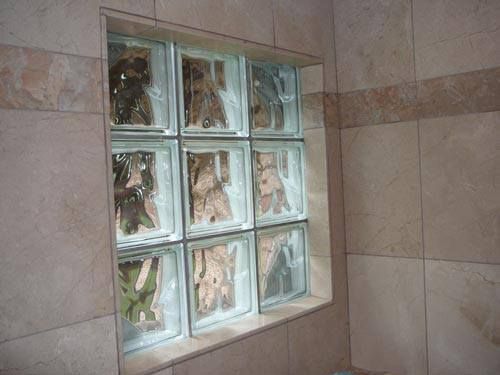 A square, 3x3 grid of glass blocks set into a wall covered in light brown, marbled tiles.
