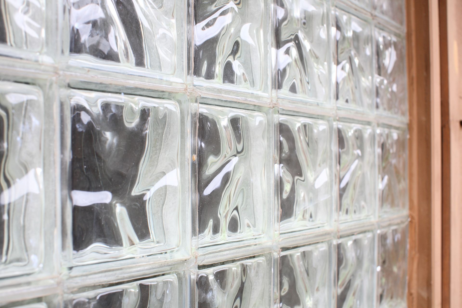 A close-up view of a wall made of translucent, wavy-patterned glass blocks set in a grid. A close-up view of a wall made of translucent, wavy-patterned glass blocks set in a grid.
