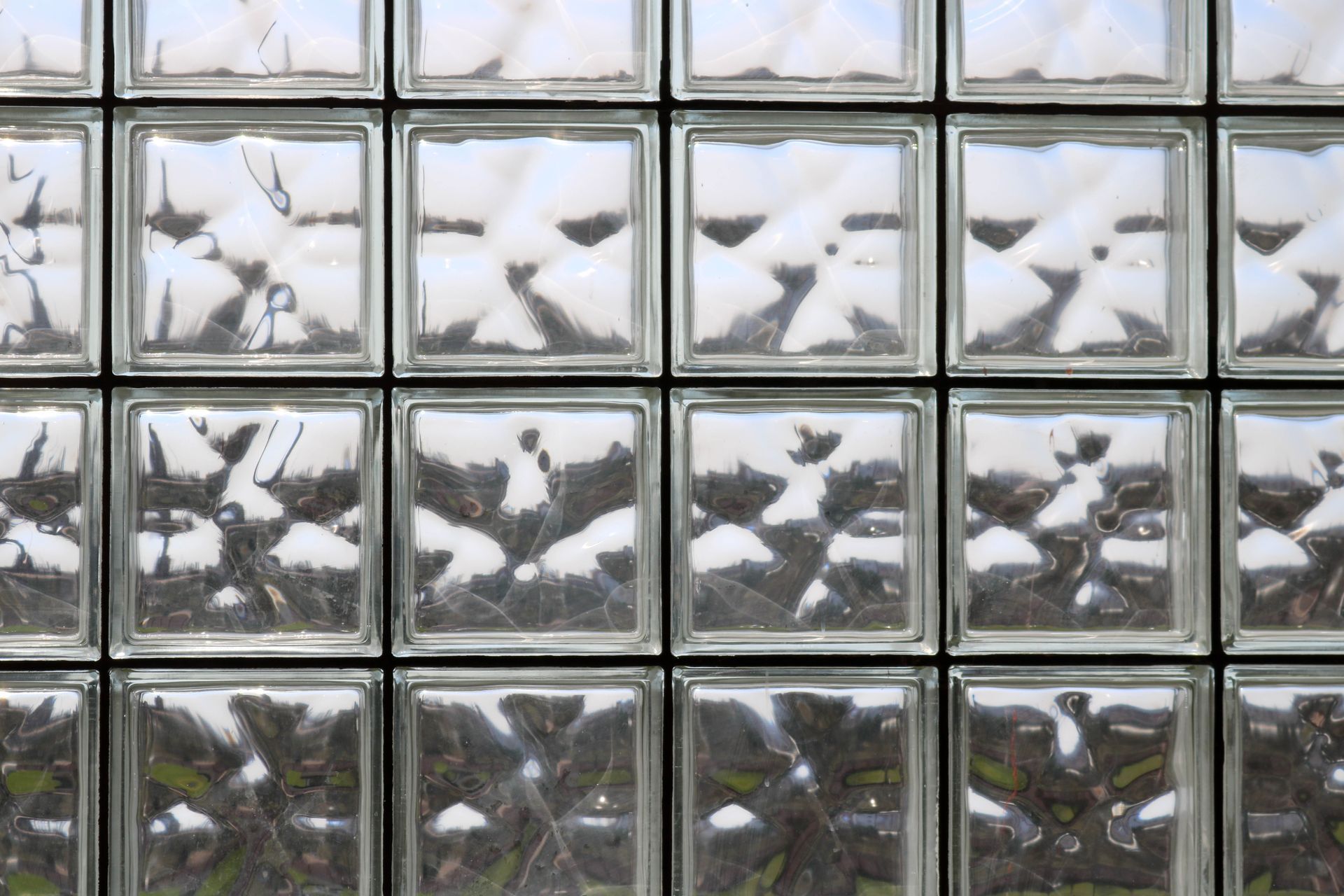 A wall constructed of square, textured glass blocks, creating a grid pattern with distorted light shining through. A wall constructed of square, textured glass blocks, creating a grid pattern with distorted light shining through.