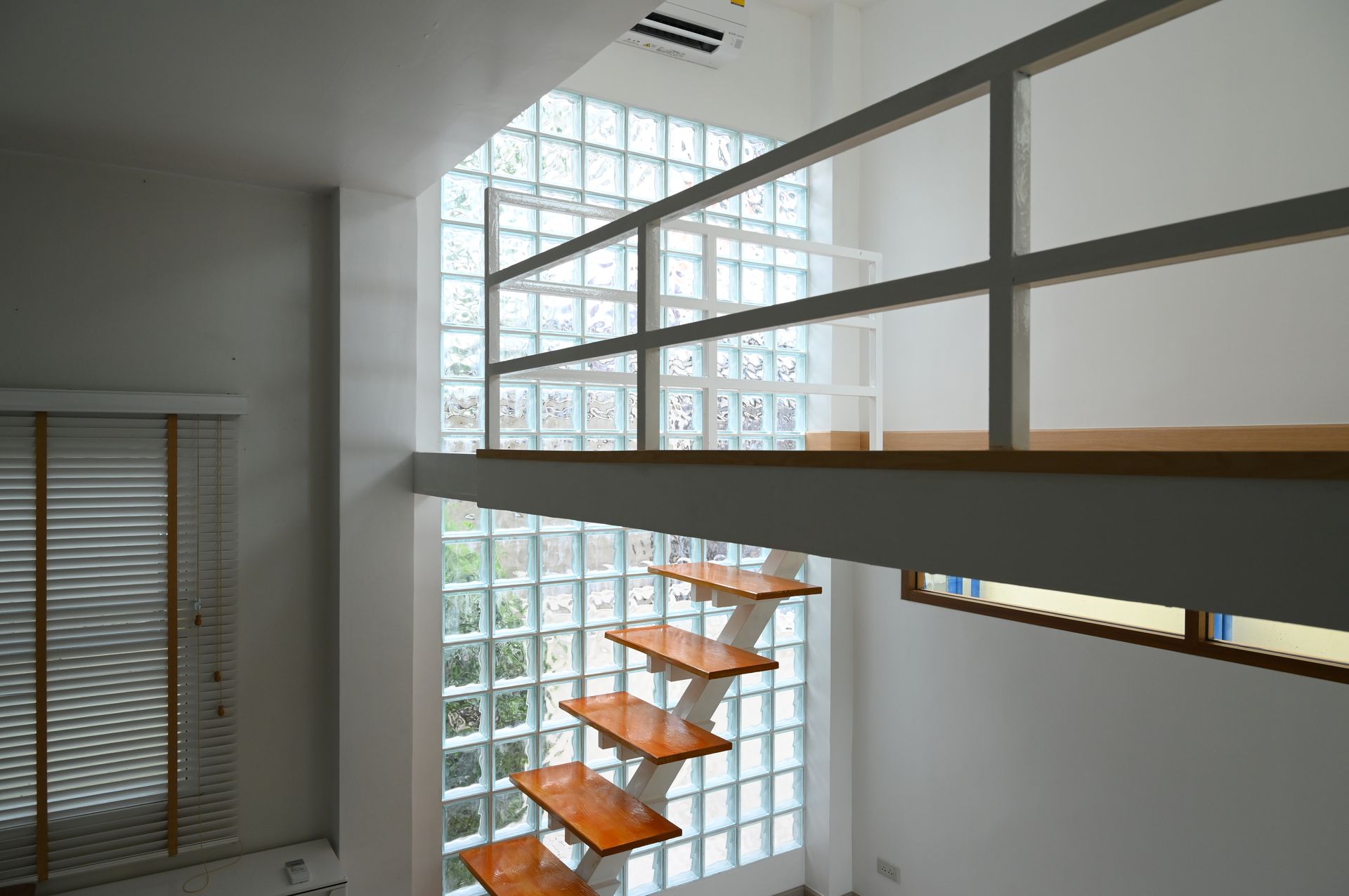 Modern interior with a floating wooden staircase, a loft level with a metal railing, and a tall glass block feature wall. Modern interior with a floating wooden staircase, a loft level with a metal railing, and a tall glass block feature wall.