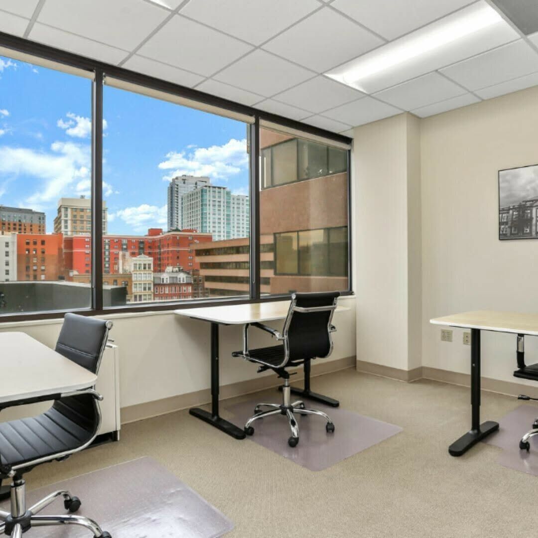 Empty modern office with desks and chairs, large windows overlooking city buildings and blue sky