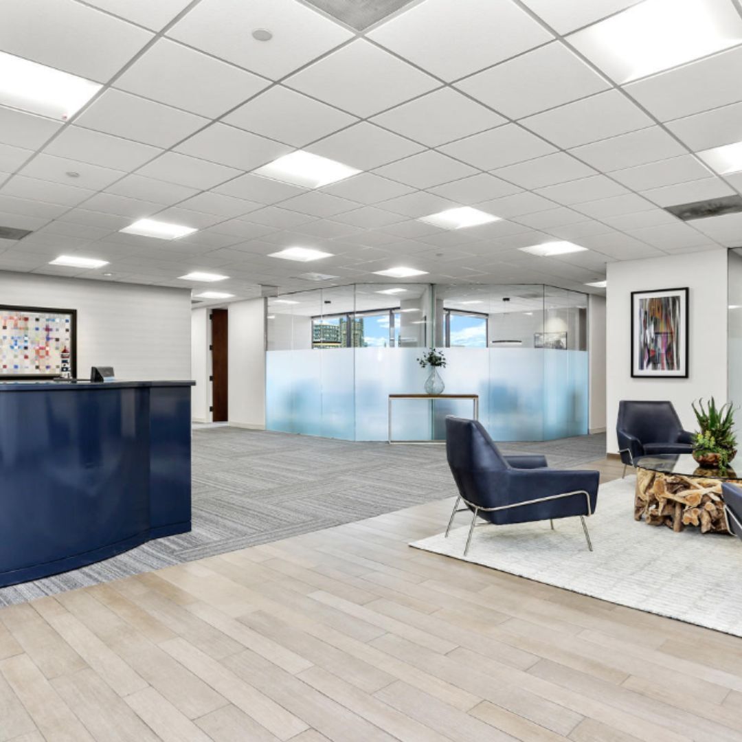 Modern office lobby with blue reception desk, glass partitions, seating area, and potted plants