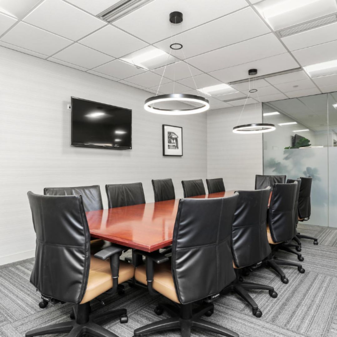 Modern conference room with a wooden table, black chairs, wall-mounted TV, and glass partitions
