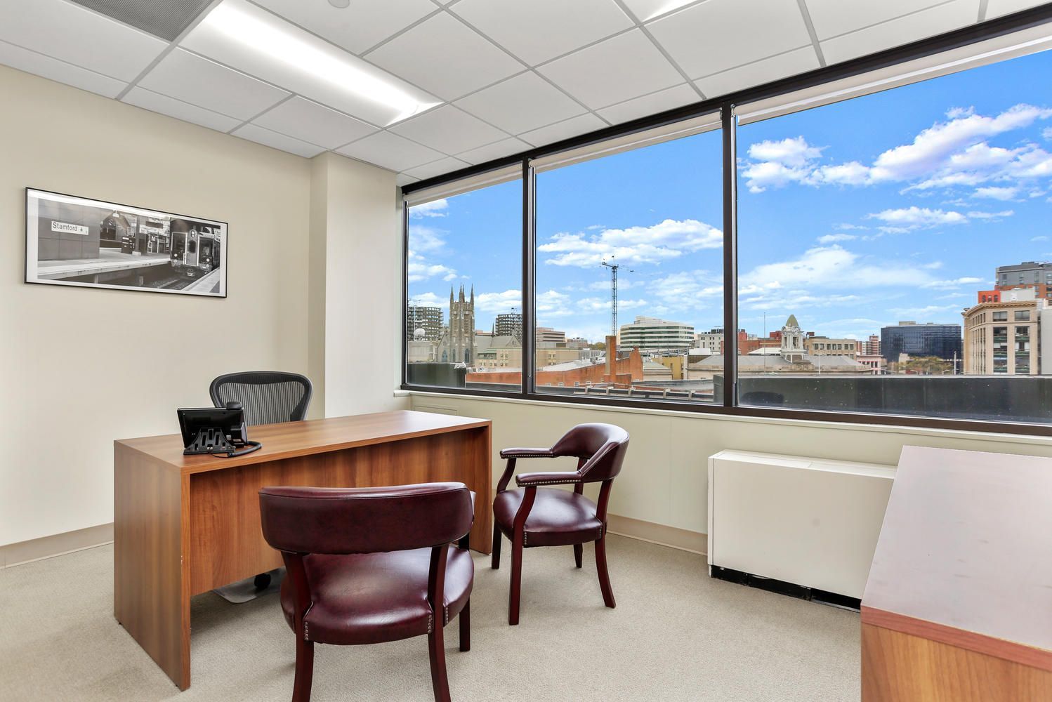 Modern office with wooden desk and chairs, large windows, city skyline view, and a black leather chair.