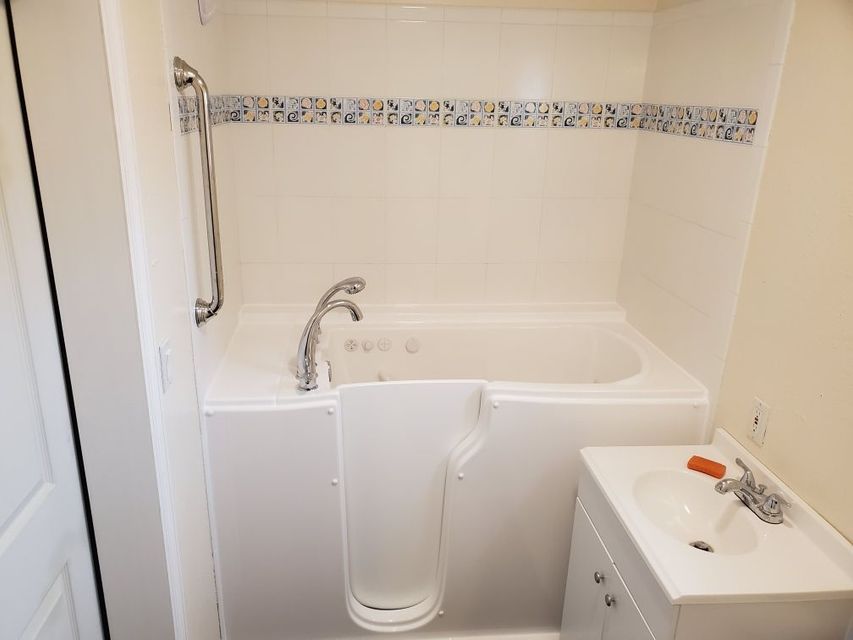Accessible bathroom with a white walk-in tub, handheld shower, and sink