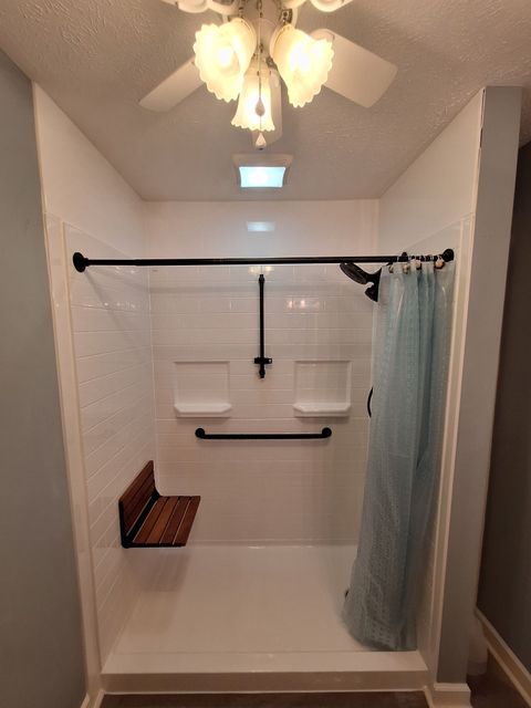 Bathroom with a white tub, grab bars, shower curtain, and overhead light fan.