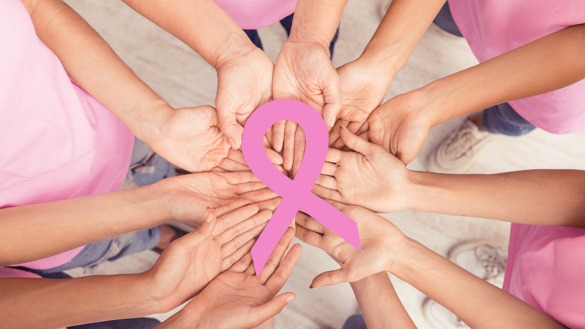 Hands holding pink ribbon, symbolizing breast cancer awareness.