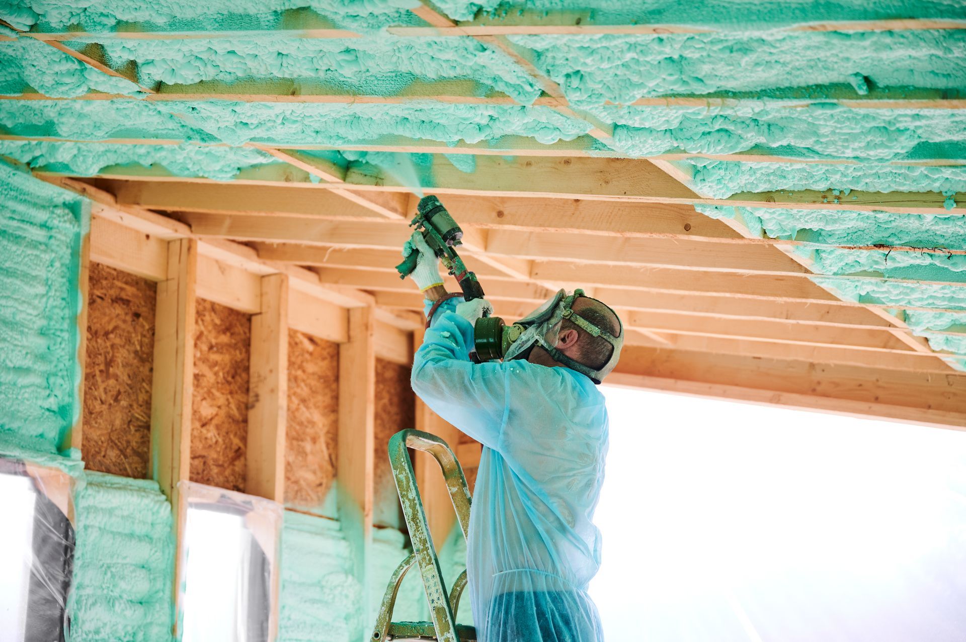 A man is spraying insulation on the ceiling of a house.