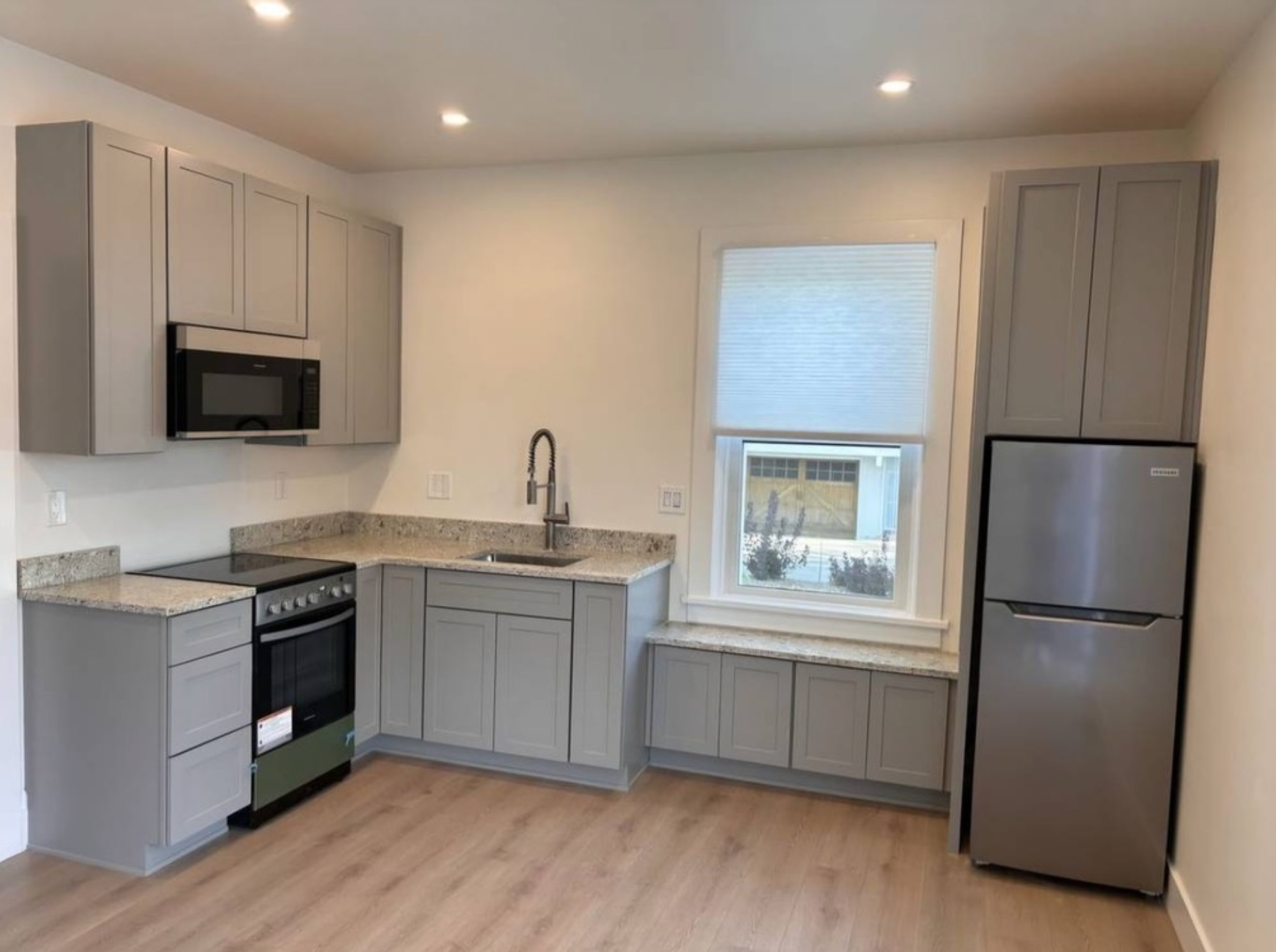 Modern kitchen with gray cabinets, stainless appliances, granite countertops, and a window above the sink