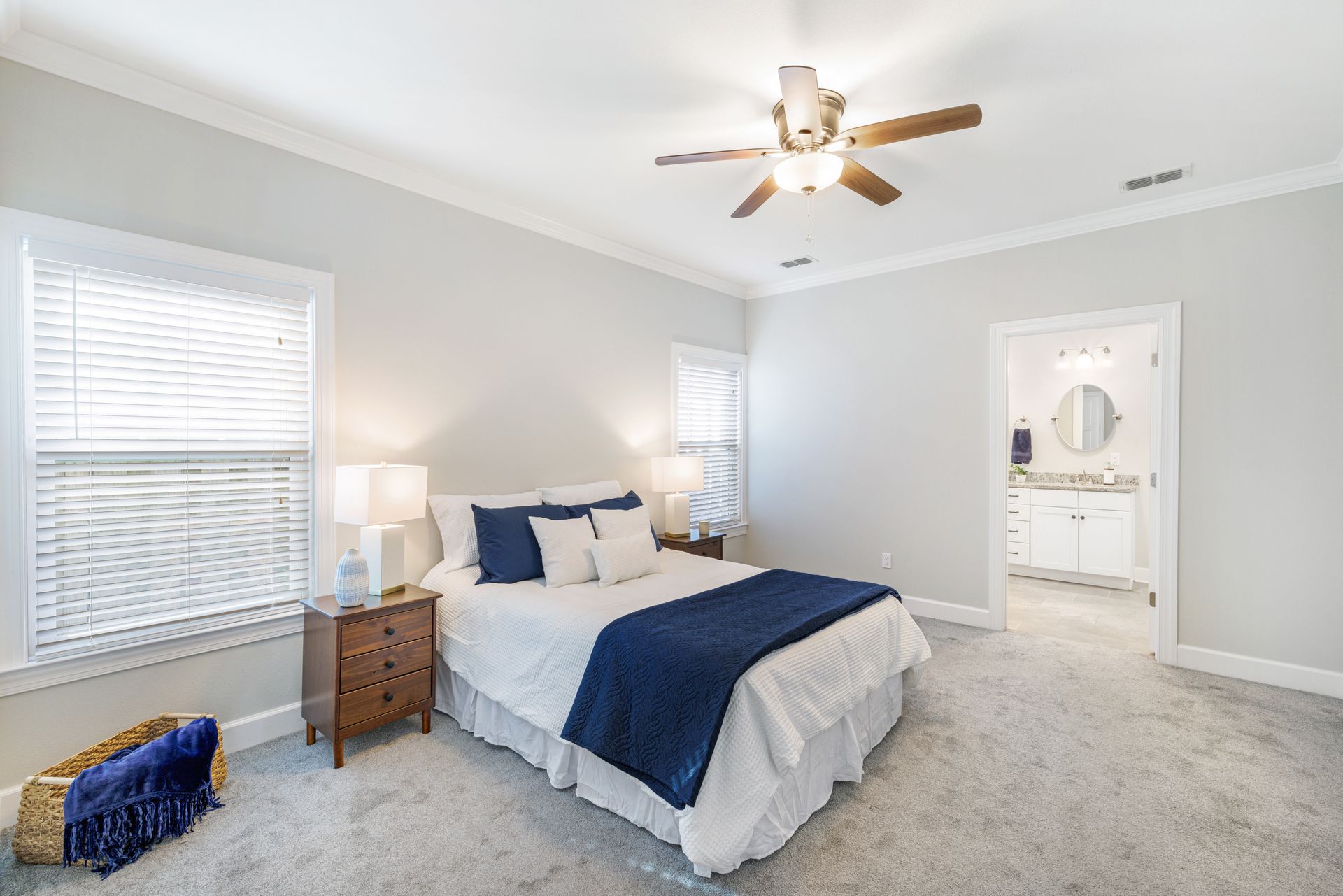 Bedroom with a bed, nightstands, windows, and a doorway to a bathroom. Light gray walls and carpet.