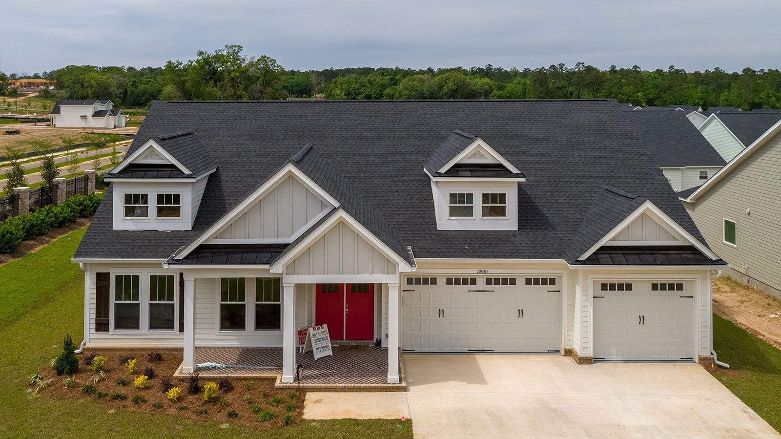 White house with black roof, red door, and three-car garage in a suburban setting.