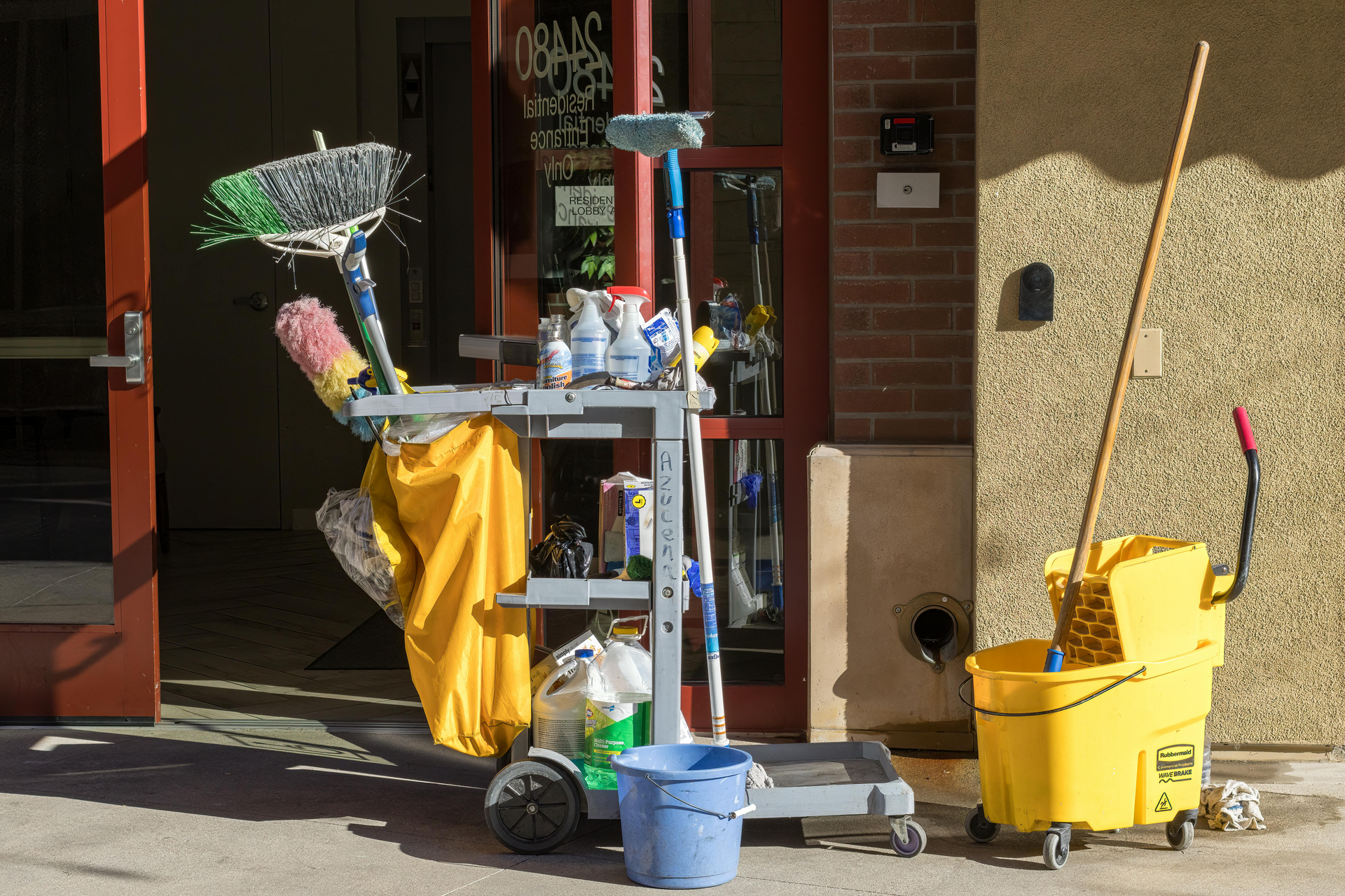 Custodial cart with mop, broom, bucket, and cleaning supplies outside a building entrance