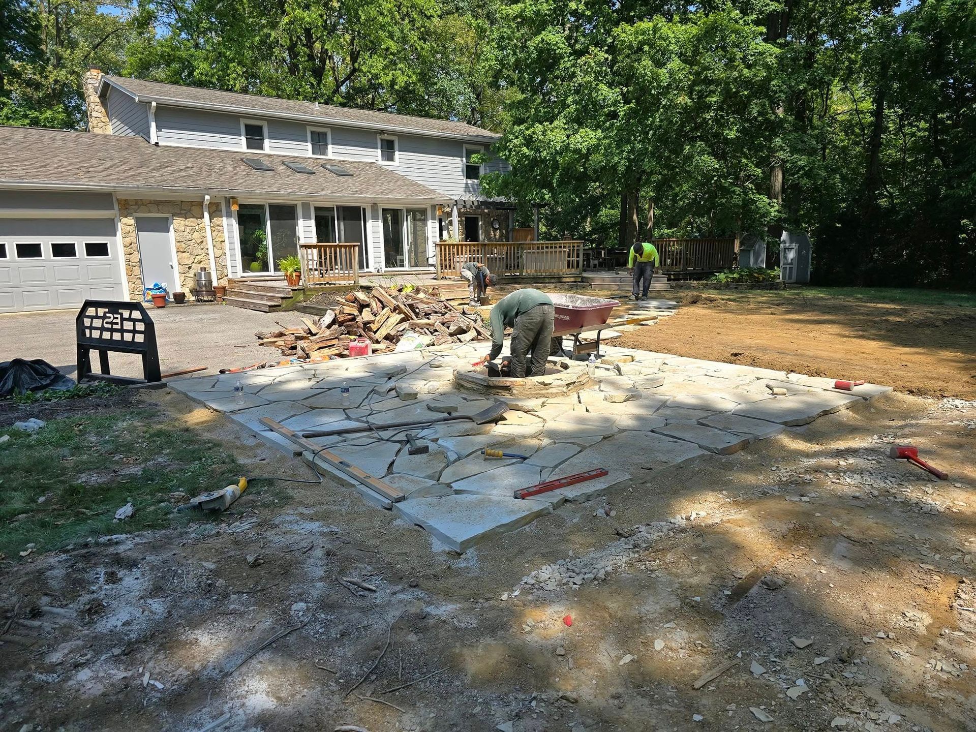 Construction workers working on a concrete patio in front of a two-story house.