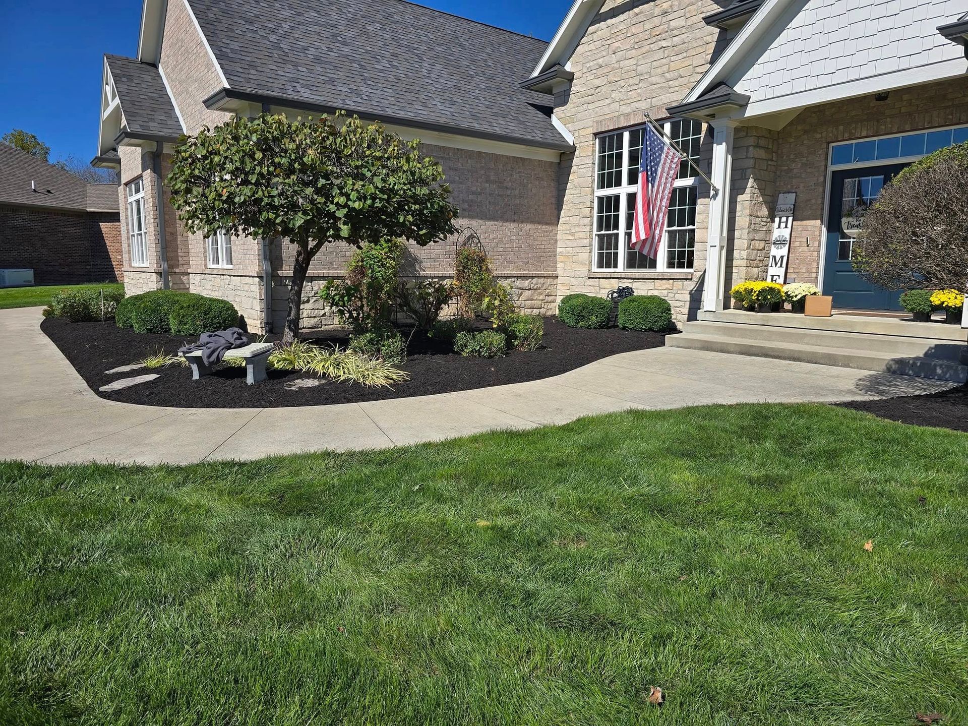 A house with a sidewalk, green lawn, and mulched landscaping. An American flag hangs on the porch.