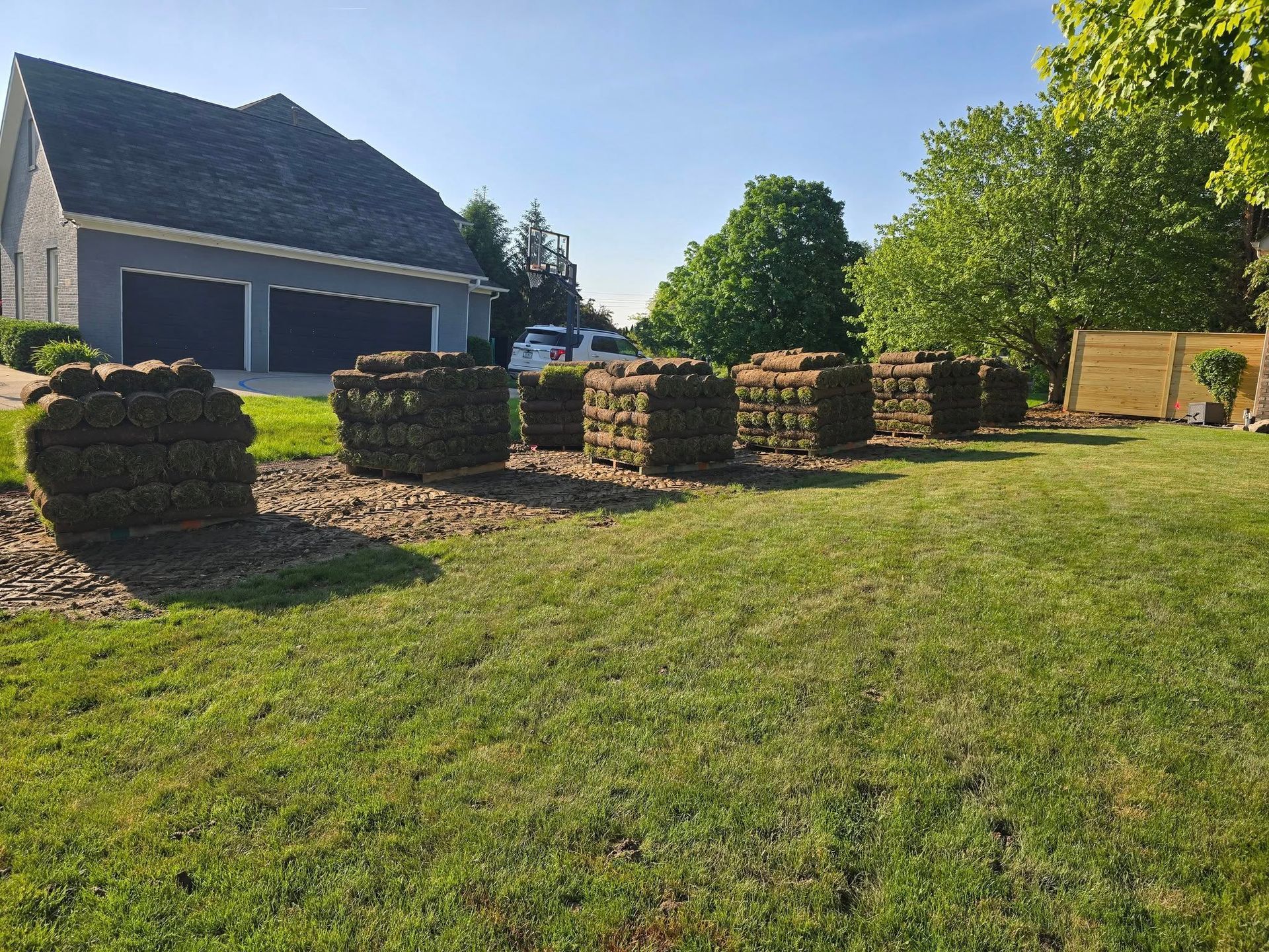 Stacks of sod on a lawn in front of a house, ready to be installed. Sunny day.