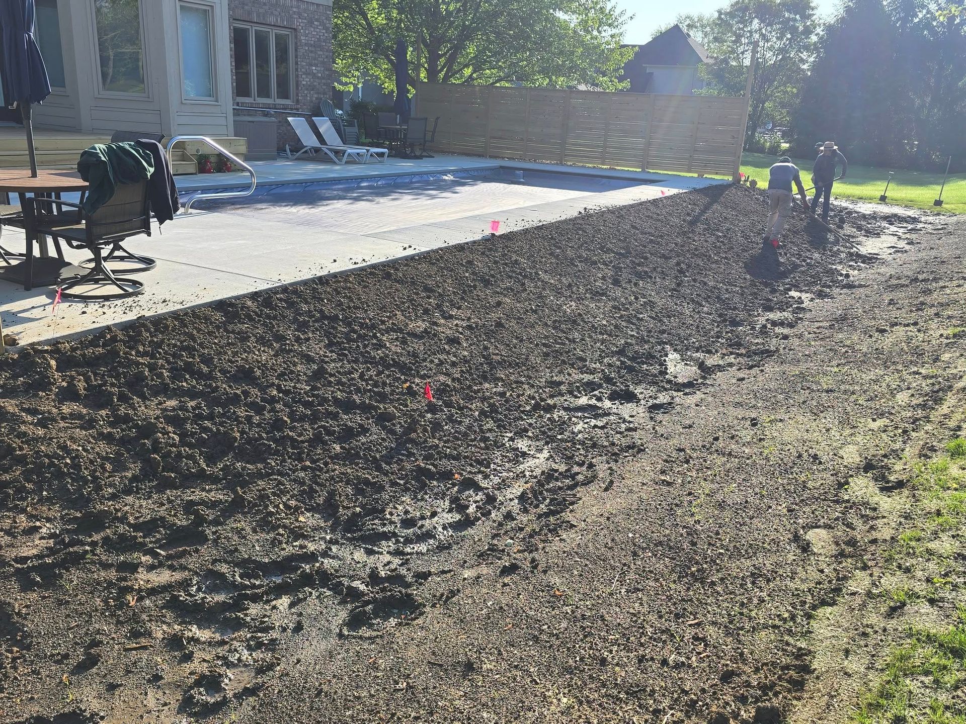 Construction of a patio area. Mud and gravel in the foreground; a concrete patio and building in the background.