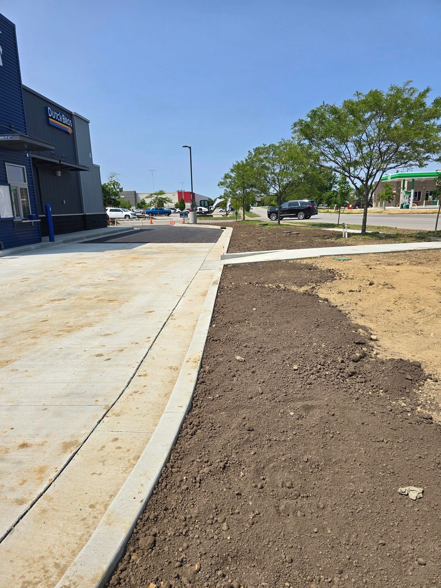 Sidewalk and dirt landscaping bed next to a commercial building, sunny day.