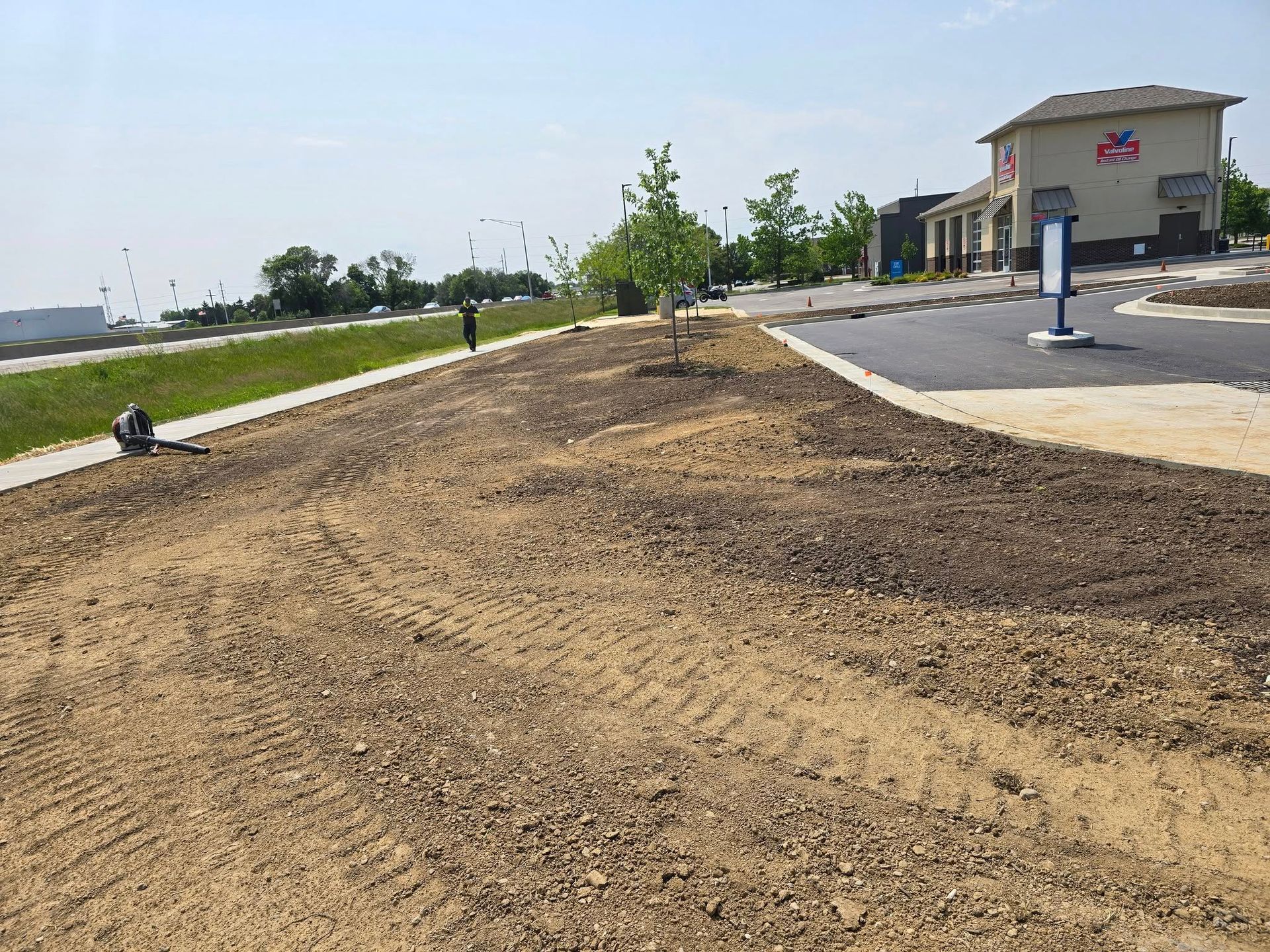 Newly landscaped area with dirt, a tree, and a building under a bright sky.