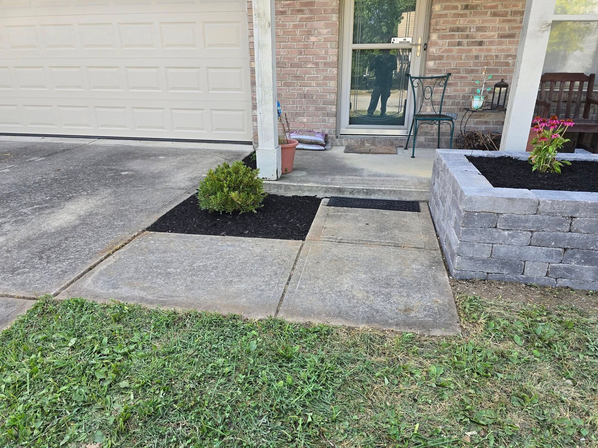 Concrete walkway leads to a front door with a small, landscaped garden bed with dark mulch and a brick retaining wall.
