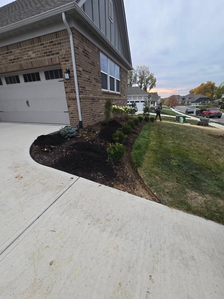 A house with a driveway and landscaped bed, green lawn, brick exterior and a garage.