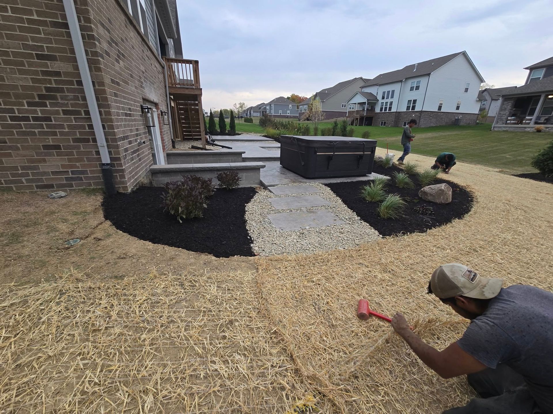 Man installing landscape mulch in a yard. House with patio and plants in the background.