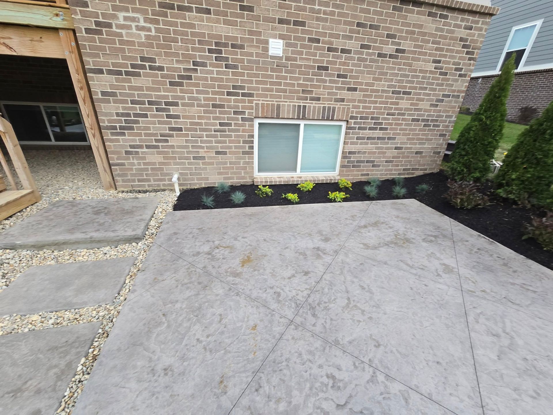 Backyard patio with stone walkway, brick wall, window, and small plants.