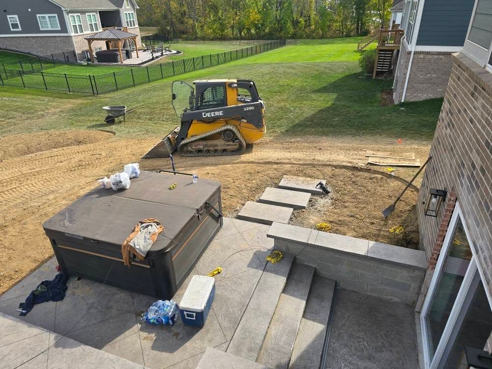 Construction site with a hot tub on a concrete patio. A skid steer works on the yard in the background.