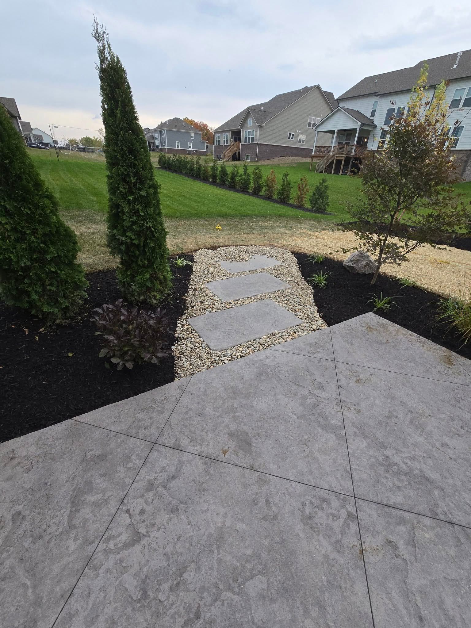 Stone path leading from a patio, through a landscaped yard, towards houses.