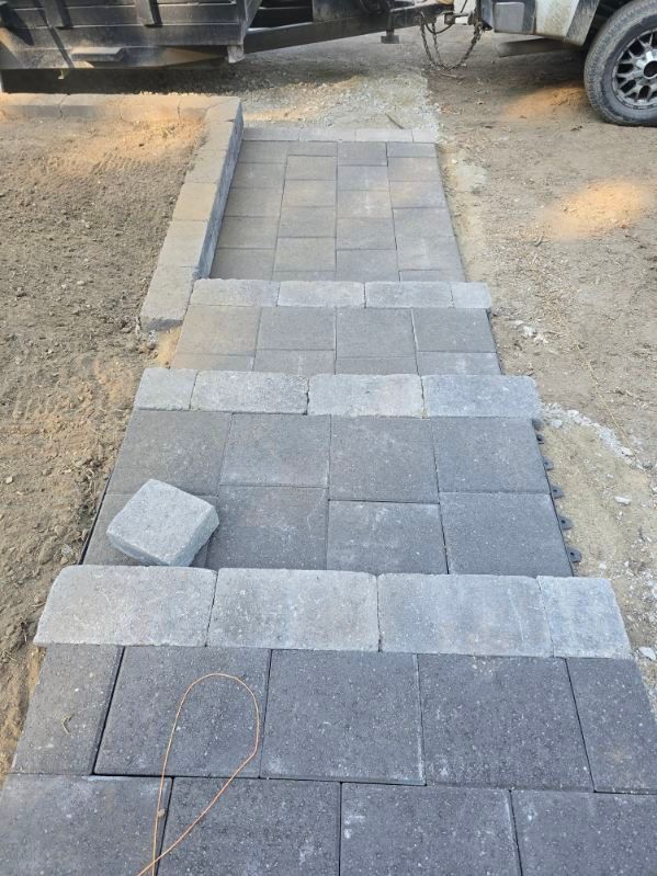 Stone pavers forming steps and a path. Gray and dark grey blocks on dirt ground, near a trailer.