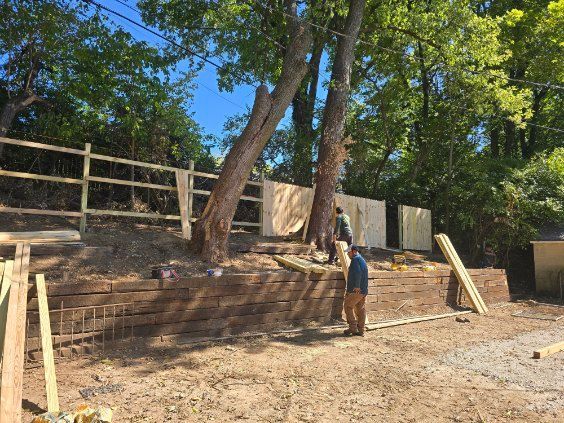 Construction site: man working on a retaining wall and wooden fence next to trees.