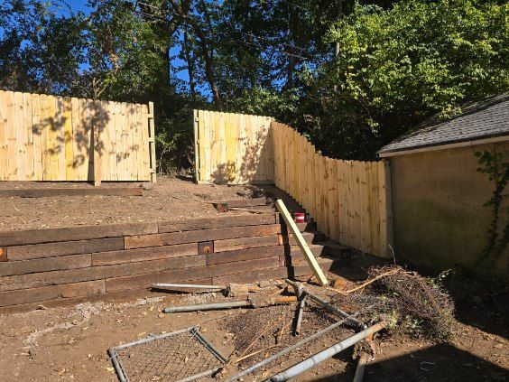 New wooden fence in backyard; earth-toned retaining wall and construction debris are in front.