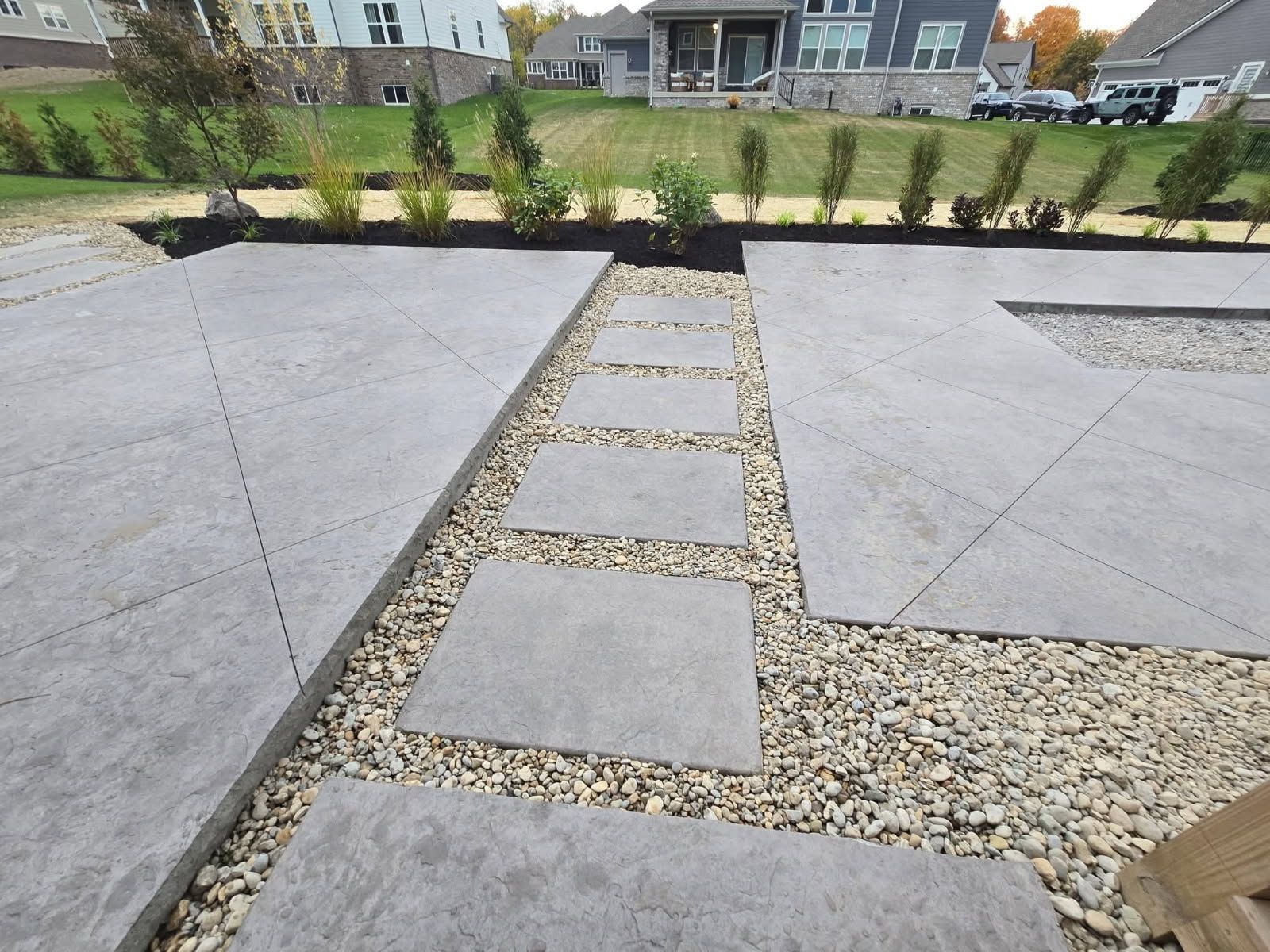 Gray stone patio with stepping stones and gravel path to backyard with landscaping.