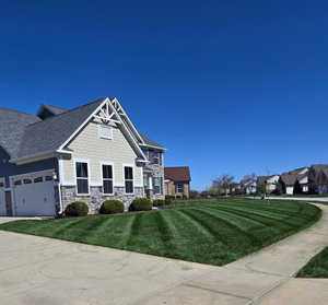 House with striped green lawn under a bright blue sky.