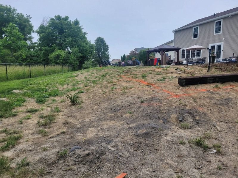 A sloped, bare backyard with orange construction markings, a house, and a fence on an overcast day.
