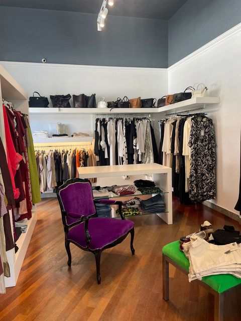 Interno di una boutique di abbigliamento con appendiabiti, scaffali e sedie viola e verdi.