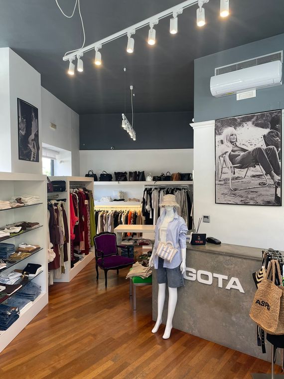 Interno di una boutique di abbigliamento con scaffali pieni di vestiti, manichini e un soffitto illuminato da faretti.
