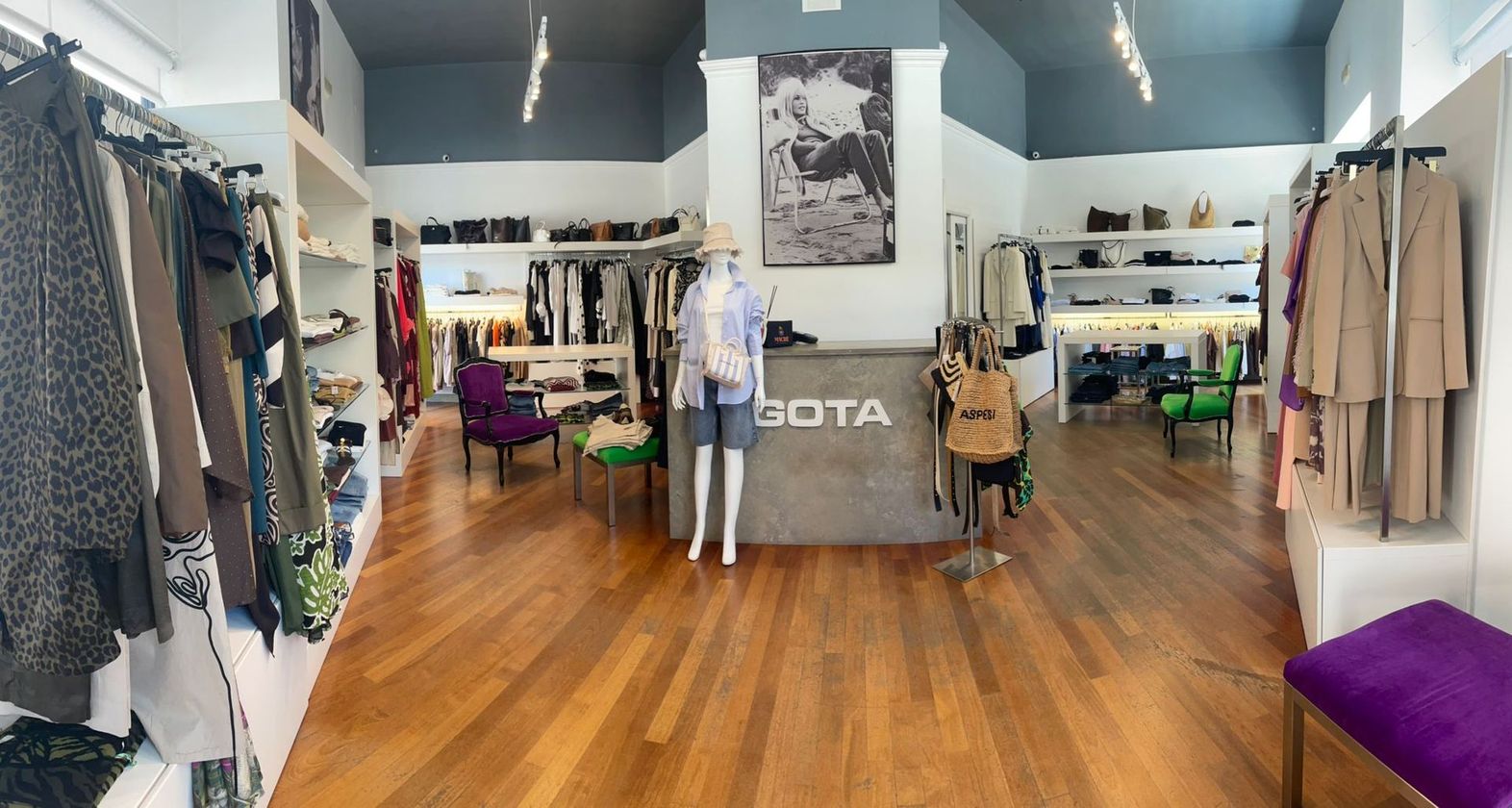 Interno di una boutique di abbigliamento con appendiabiti, un manichino e pavimenti in legno lucido.